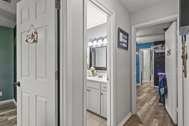 hallway featuring visible vents, a sink, a textured ceiling, light wood-type flooring, and baseboards