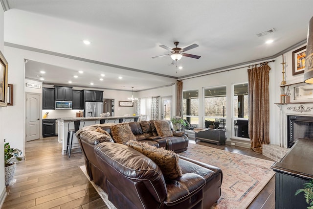 living area featuring visible vents, ceiling fan with notable chandelier, light wood-style floors, a fireplace, and recessed lighting