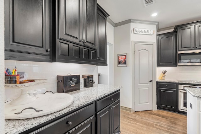 kitchen featuring visible vents, light stone counters, stainless steel appliances, light wood-type flooring, and backsplash