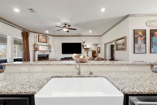 kitchen featuring arched walkways, visible vents, ornamental molding, open floor plan, and a sink