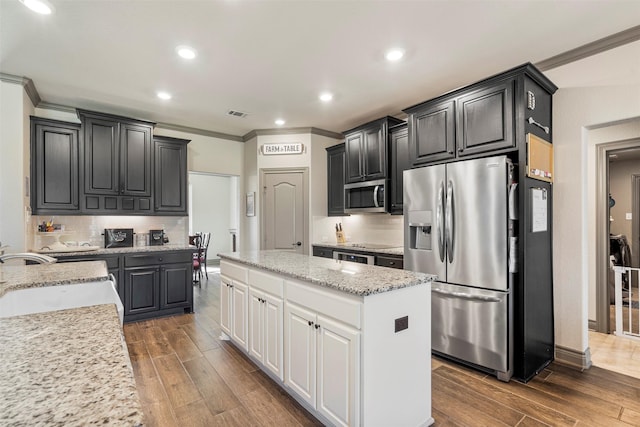 kitchen featuring stainless steel appliances, ornamental molding, wood tiled floor, a sink, and a kitchen island