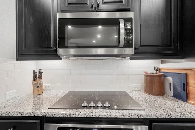 kitchen featuring dark cabinetry, stainless steel microwave, backsplash, and black electric cooktop