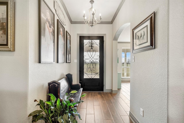 foyer featuring arched walkways, a textured wall, an inviting chandelier, ornamental molding, and wood finished floors