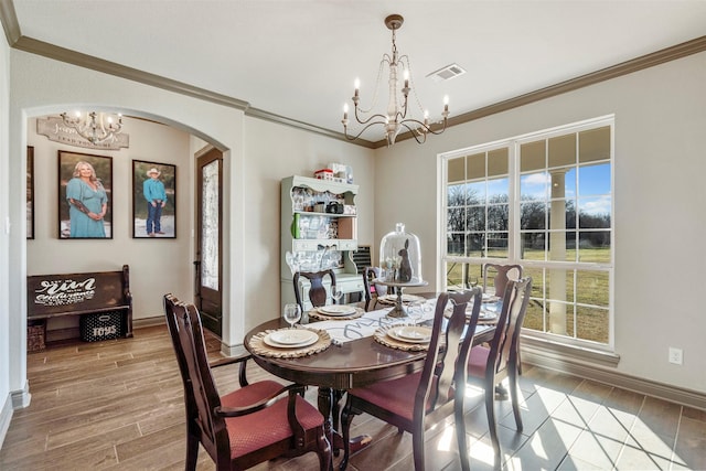 dining room featuring light wood-style floors, a chandelier, arched walkways, and ornamental molding