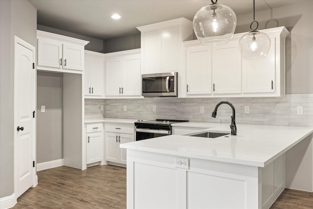 kitchen featuring wood finished floors, a peninsula, light countertops, stainless steel appliances, and a sink