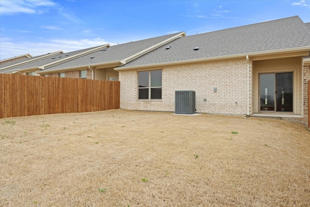 back of property with a shingled roof, cooling unit, brick siding, and fence