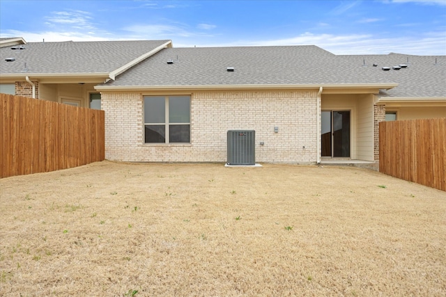 back of house featuring roof with shingles, brick siding, fence, and central air condition unit