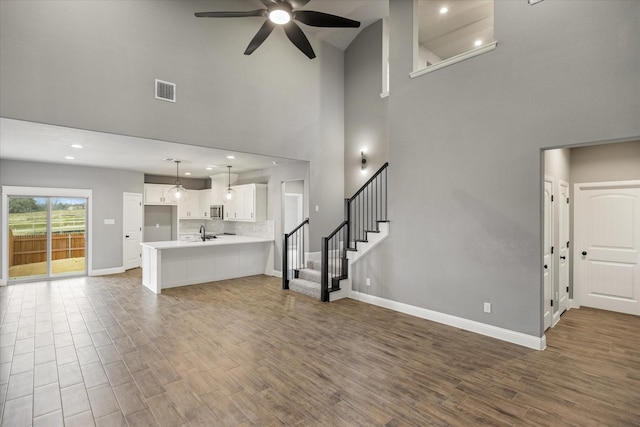 unfurnished living room with ceiling fan, wood finished floors, visible vents, baseboards, and stairway