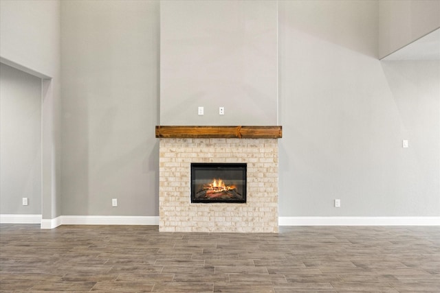 unfurnished living room with a brick fireplace, wood finished floors, and baseboards