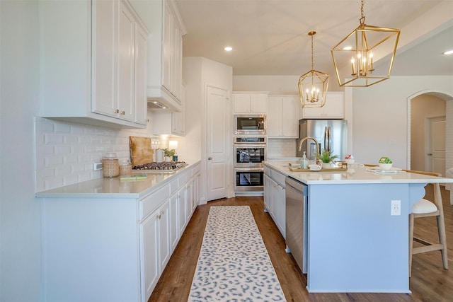 kitchen featuring arched walkways, white cabinets, dark wood finished floors, appliances with stainless steel finishes, and a sink