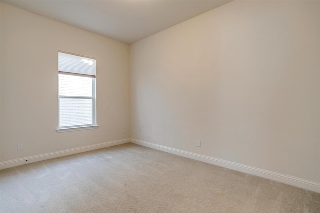 spare room with baseboards and light colored carpet