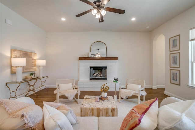 living room with arched walkways, recessed lighting, wood finished floors, baseboards, and a brick fireplace