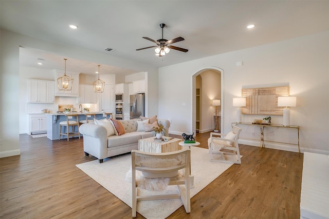 living area featuring baseboards, visible vents, arched walkways, ceiling fan, and wood finished floors