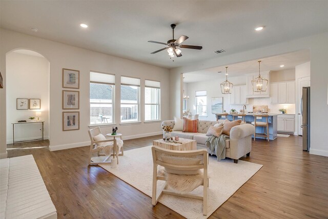 living area featuring arched walkways, dark wood-type flooring, ceiling fan with notable chandelier, and visible vents