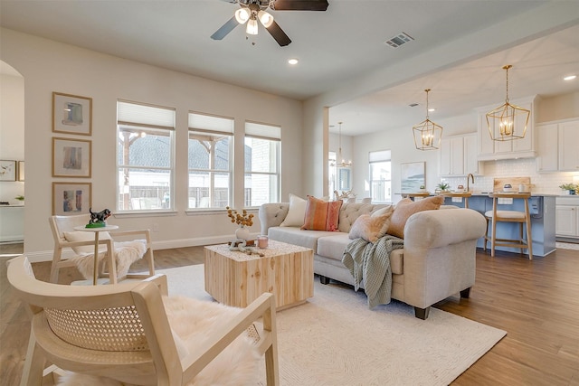 living room with recessed lighting, ceiling fan with notable chandelier, visible vents, baseboards, and light wood-style floors