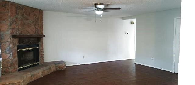 unfurnished living room featuring a textured ceiling, a fireplace, wood finished floors, and a ceiling fan