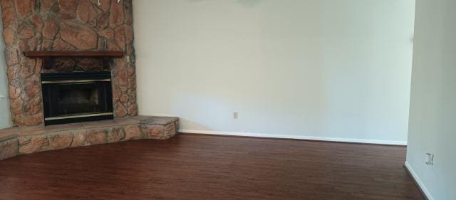 unfurnished living room featuring baseboards, wood finished floors, and a stone fireplace