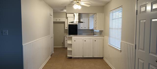 kitchen featuring light tile patterned floors, white cabinets, a wainscoted wall, wall chimney range hood, and black oven