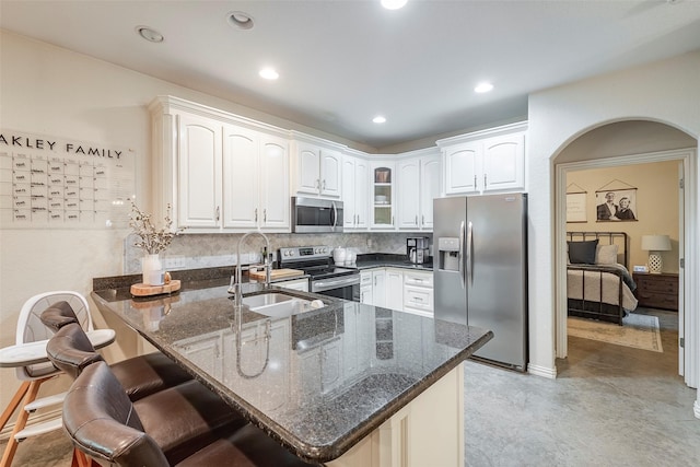 kitchen featuring arched walkways, stainless steel appliances, a sink, dark stone countertops, and a peninsula