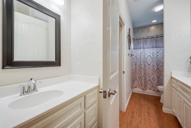 full bath with toilet, a textured wall, wood finished floors, and vanity