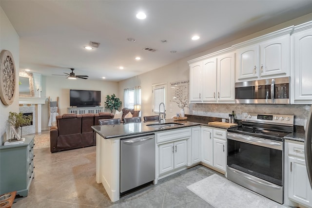 kitchen featuring a fireplace, decorative backsplash, appliances with stainless steel finishes, a sink, and a peninsula