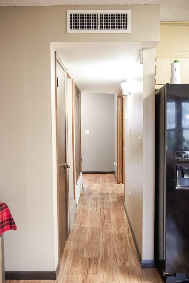 hall with light wood-style floors, baseboards, visible vents, and a textured ceiling