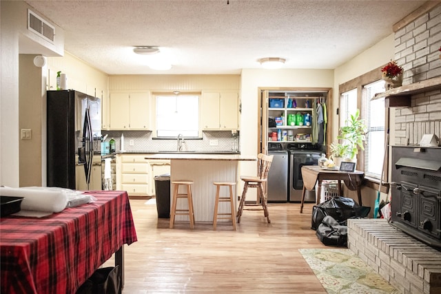 kitchen with a breakfast bar area, visible vents, open floor plan, independent washer and dryer, and black fridge