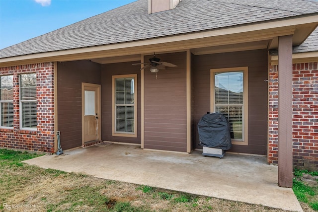 property entrance featuring a patio area, a shingled roof, a ceiling fan, and brick siding