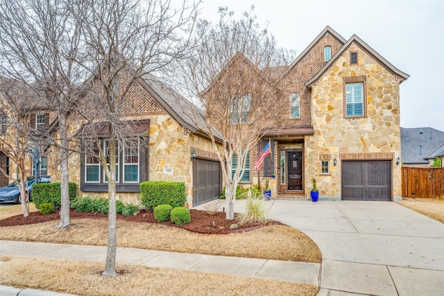 view of front facade with an attached garage, stone siding, fence, and concrete driveway