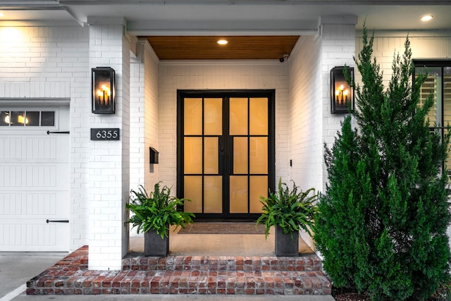 entrance to property featuring an attached garage, french doors, and brick siding