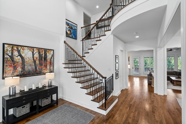 staircase featuring baseboards, ceiling fan, wood finished floors, a high ceiling, and recessed lighting