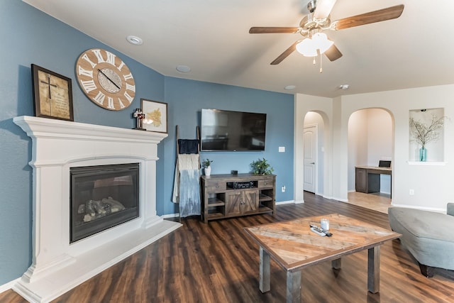 living room with baseboards, arched walkways, a glass covered fireplace, ceiling fan, and wood finished floors