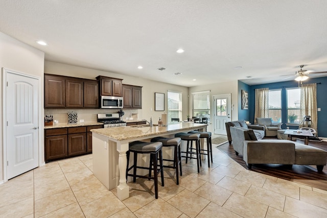 kitchen with a breakfast bar area, open floor plan, a kitchen island with sink, stainless steel appliances, and dark brown cabinets