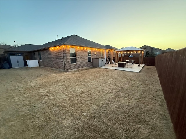 back of property at dusk with a patio, brick siding, and a fenced backyard