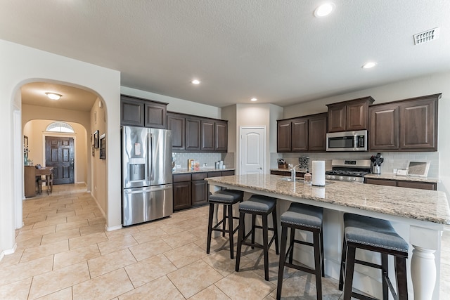 kitchen featuring arched walkways, stainless steel appliances, a breakfast bar, visible vents, and dark brown cabinets