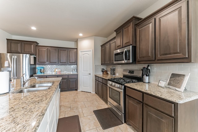 kitchen with stainless steel appliances, a sink, dark brown cabinets, and light stone countertops