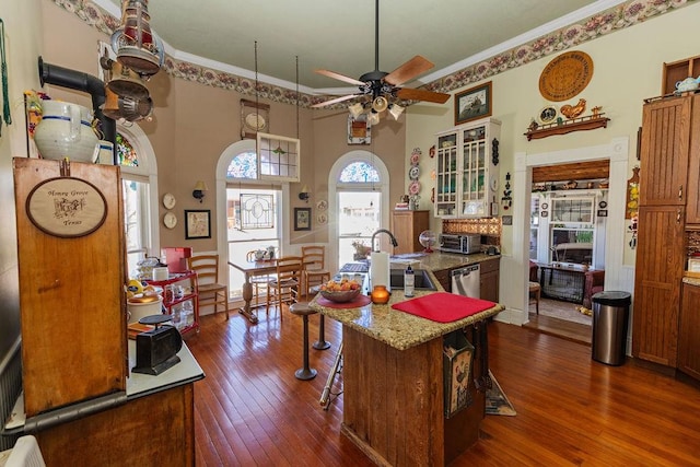 kitchen with brown cabinetry, dark wood finished floors, a kitchen island with sink, dishwasher, and crown molding