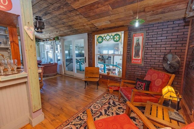 sitting room featuring wood finished floors, plenty of natural light, wooden ceiling, and brick wall