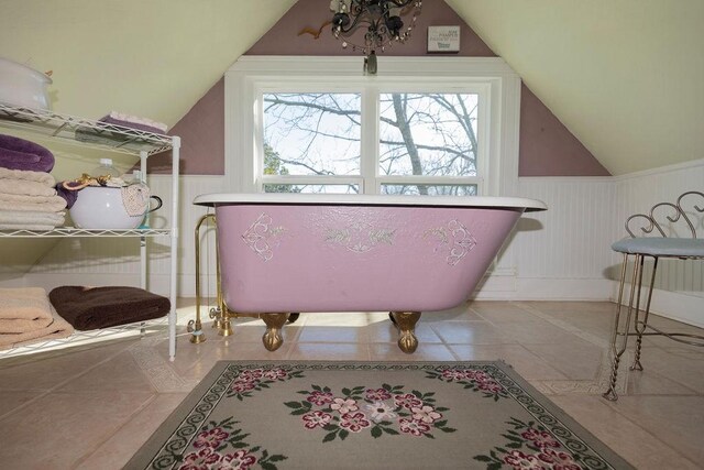 bathroom featuring tile patterned floors, a freestanding tub, wainscoting, and vaulted ceiling