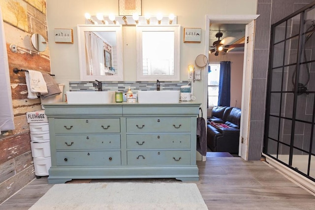 ensuite bathroom with double vanity, wood finished floors, tasteful backsplash, and a sink