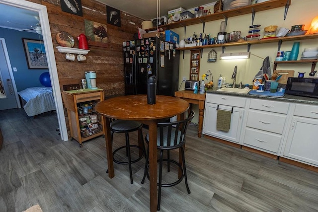 bar with wooden walls, a ceiling fan, a sink, black appliances, and dark wood-type flooring