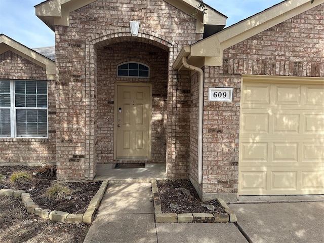 view of exterior entry with brick siding and an attached garage