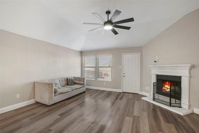 unfurnished living room with wood finished floors, baseboards, a warm lit fireplace, ceiling fan, and vaulted ceiling