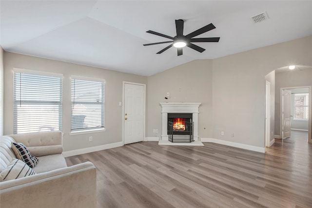 unfurnished living room with light wood-type flooring, visible vents, a warm lit fireplace, arched walkways, and lofted ceiling