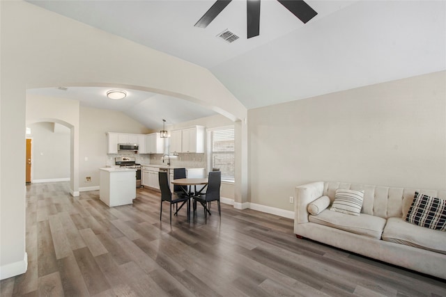 living area featuring light wood-style floors, vaulted ceiling, arched walkways, and visible vents