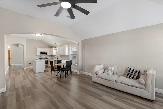 living area featuring arched walkways, baseboards, light wood-type flooring, and lofted ceiling