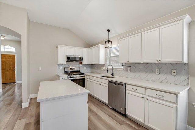 kitchen with a center island, vaulted ceiling, appliances with stainless steel finishes, arched walkways, and a sink