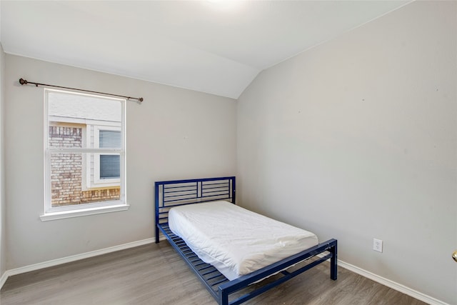 bedroom with vaulted ceiling, wood finished floors, and baseboards