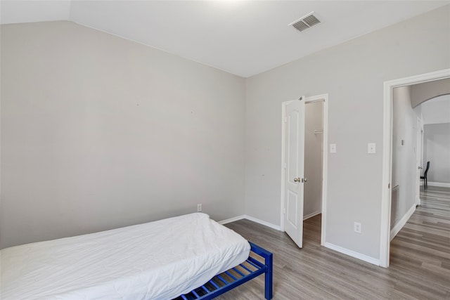 bedroom with visible vents, wood finished floors, baseboards, arched walkways, and lofted ceiling