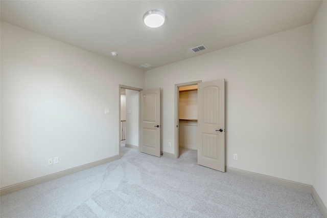 unfurnished bedroom with light carpet, baseboards, visible vents, and a walk in closet